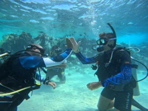 Open Water Diver students celebrating with high five underwater during course at Marsa Samadai with Deep South Divers